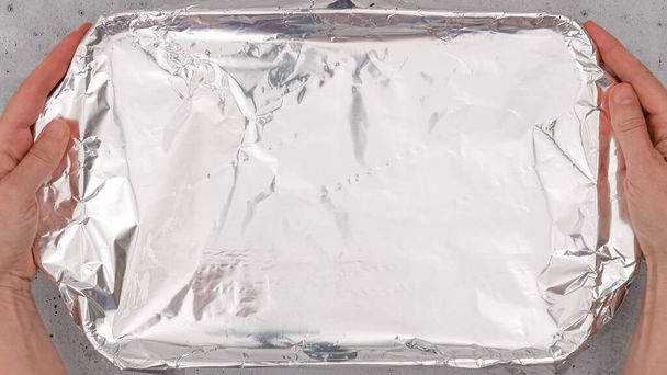 Baking dish covered with aluminum foil close up on the table. Spinach lasagna recipe. Before baking cover lasagna with aluminum foil. - Photo, Image