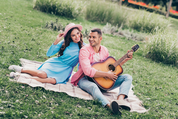 Photo of young two students couple lovers sitting grass in park guy playing music guitar instrumental. - Photo, Image
