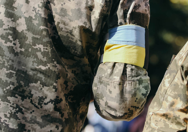  Ein ukrainischer Soldat mit einem gelb-blauen Band am Arm (die Flagge der Ukraine) bei der Verabschiedung ukrainischer Soldaten, die während des Krieges mit Russland gefallen sind - Foto, Bild
