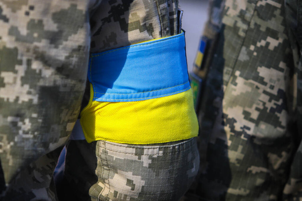  Un soldado ucraniano con una cinta amarilla-azul en el brazo (la bandera de Ucrania) durante una despedida de los soldados ucranianos que murieron durante la guerra con Rusia - Foto, Imagen