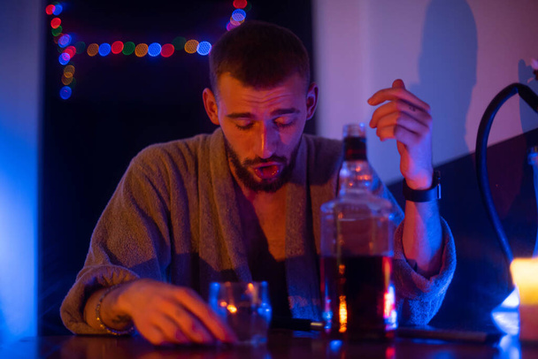 Egy köpenyes, szakállas férfi ül a vízipipában. Whiskyt iszik és vízipipát szív.. - Fotó, kép