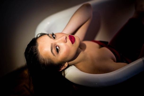 Fascinating brunette lies in the bathroom in a red dress. Looks at the camera. Close up. - Foto, afbeelding