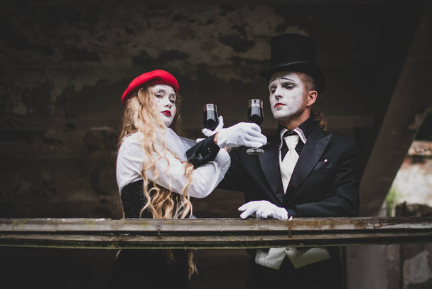 The hatter and alice in wonderland. A girl with long hair in a red hat with white makeup on her face. A man in a suit with make-up and a black hat. They drink wine. Halloween - Fotó, kép