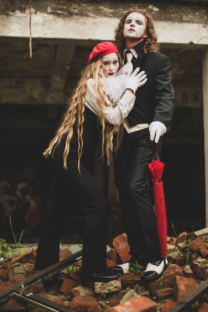 Дівчина в чорно-білому костюмі в червоному береті з макіяжем спирається на високого молодого чоловіка в чорному костюмі і капелюсі. Святкування, Хелловін
 - Фото, зображення