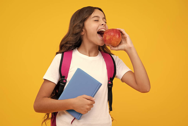 Koululainen, teini opiskelija tyttö reppu pidä omena ja kirja eristetty keltainen. Hämmästyttävä teinityttö. Innoissaan ilme, iloinen ja iloinen - Valokuva, kuva