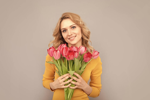 χαμογελαστή κυρία κρατήστε τα λουλούδια για τις διακοπές άνοιξη σε γκρι φόντο. - Φωτογραφία, εικόνα