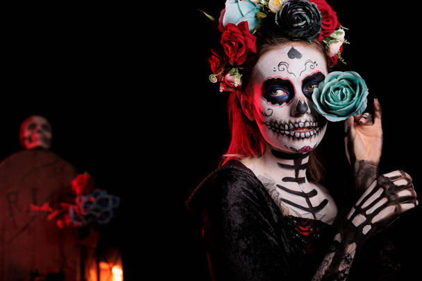 Dios de los muertos череп женщины с боди-артом, празднующей традицию февральских праздников в костюме санта-муми. Позирование с розами и фестивальным макияжем, венец цветов на фоне студии. - Фото, изображение
