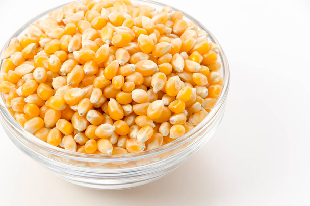 Niet-gepopte popcorn zaden in transparante glazen schaal op witte achtergrond.  - Foto, afbeelding