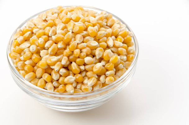Unpopped popcorn seeds in transparent glass bowl on white background.  - 写真・画像