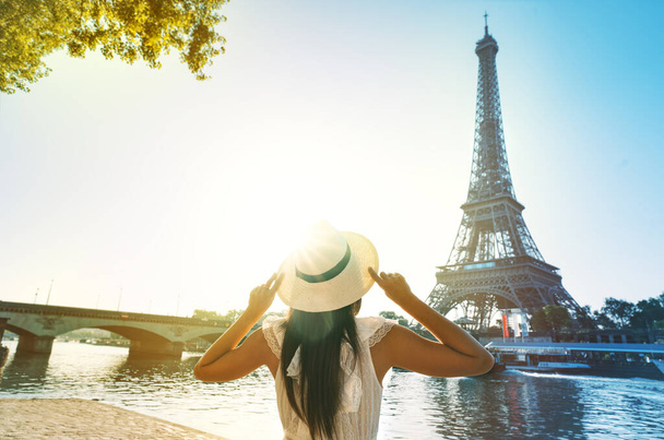 Joven turista con sombrero de sol y vestido blanco de pie frente a la Torre Eiffel en París al atardecer. Viajar en Francia, concepto de turismo. Foto de alta calidad - Foto, imagen