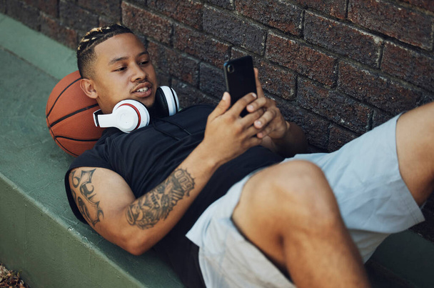 バスケットボール選手、携帯電話やフィットネスアプリは、スポーツの試合、ゲームやボールと黒の男の屋外での練習後に休憩中。スポーツや運動後のソーシャルメディア上で5gネットワークを持つ男性フィットネス選手. - 写真・画像
