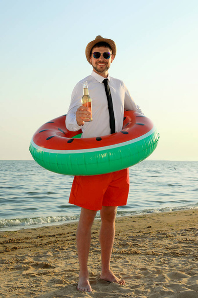 Happy man with inflatable ring and beer on beach. Business trip - 写真・画像