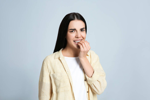 Young woman biting her nails on light grey background - Foto, afbeelding