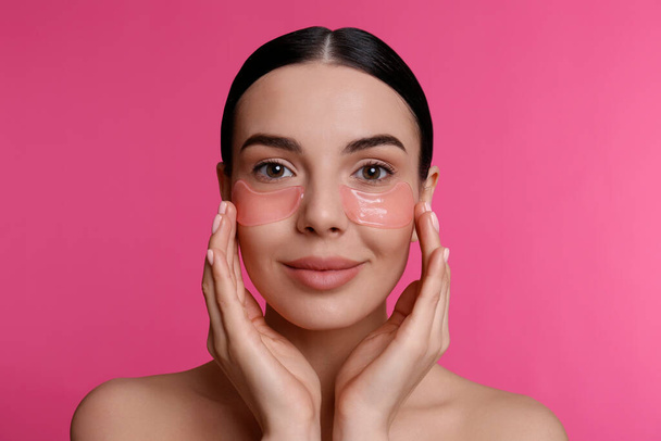 Beautiful young woman with under eye patches on pink background - Фото, изображение