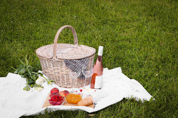 Picnic blanket with tasty food, flowers, basket and cider on green grass outdoors - Valokuva, kuva