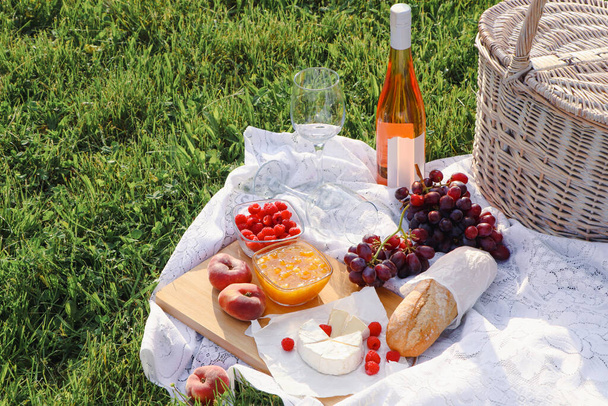 Picnic blanket with tasty food, basket and cider on green grass outdoors - Fotó, kép