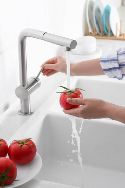 Woman washing fresh ripe tomato under tap water in kitchen, closeup - Photo, image