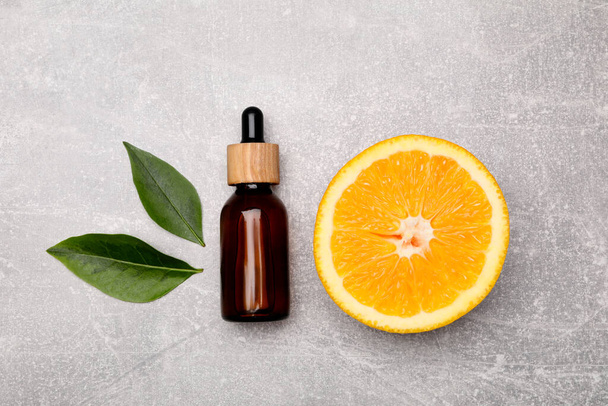 Bottle of essential oil with orange slice and leaves on grey table, flat lay - Photo, image