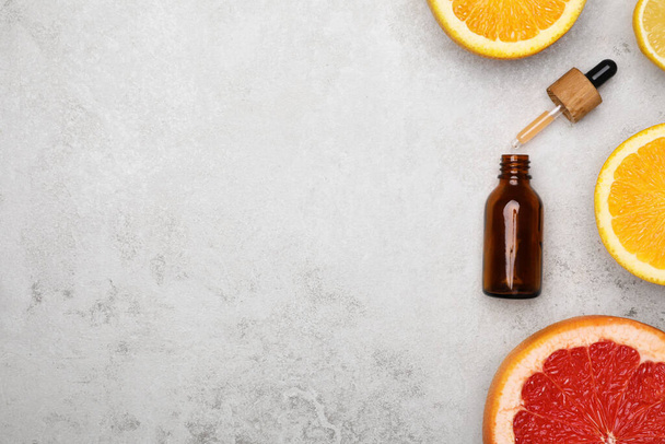 Bottle of citrus essential oil and fresh fruits on light table, flat lay. Space for text - Фото, зображення