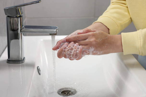 Woman washing hands with water from tap in bathroom, closeup - 写真・画像
