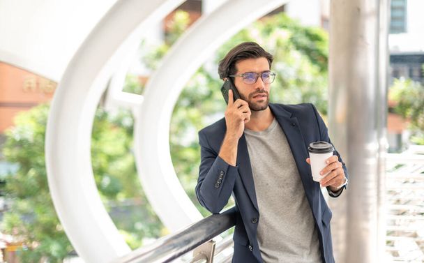 O homem segurando uma xícara de café e usando um smartphone e conversando com seu amigo enquanto ele espera por seu amigo no aeroporto. - Foto, Imagem