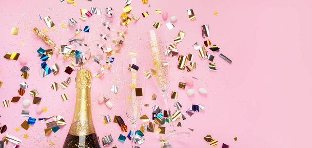Champagne bottle with confetti on pink background. Holiday decoration and party streamers on gold festive. Creative concept. Top view, copy space, panorama - Foto, immagini