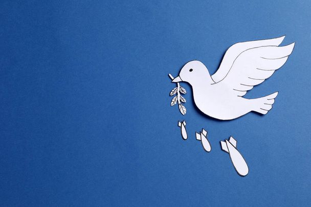 White paper dove with olive branch and bombs on blue background, flat lay. Space for text - Φωτογραφία, εικόνα