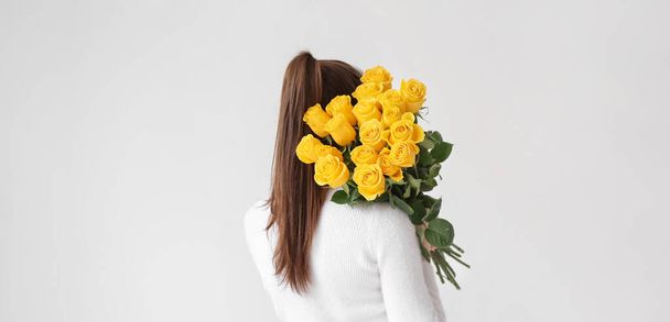 Hübsche Frau mit schönen gelben Rosen auf hellem Hintergrund - Foto, Bild