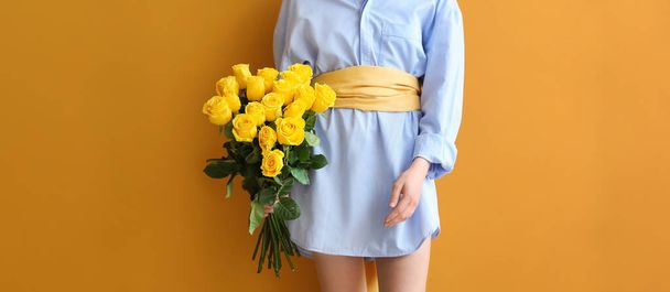 オレンジの背景に美しい黄色のバラを持つスタイリッシュな若い女性 - 写真・画像