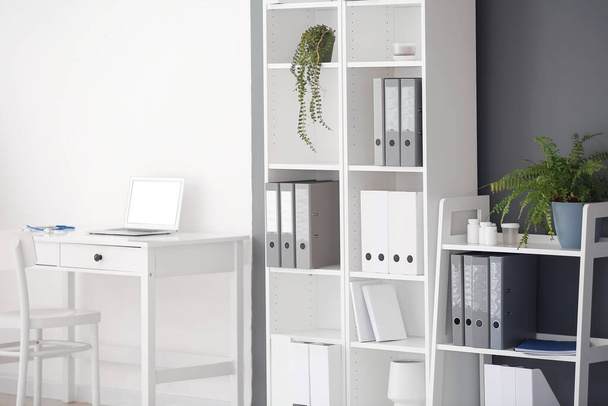 Workplace with modern laptop and shelf units in medical office - Фото, изображение