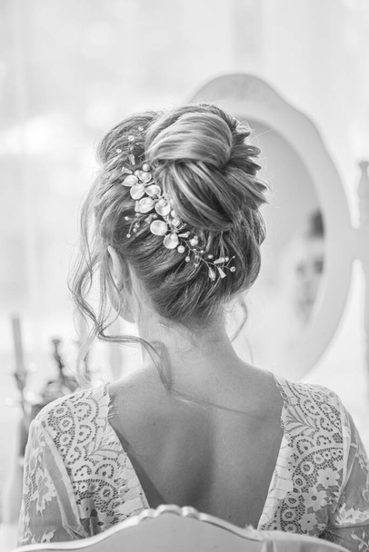 Young beautiful bride with wedding bridal hairstyle with pearls and crystals  near the boudoir table in the bedroom. wedding morning - Foto, Imagen