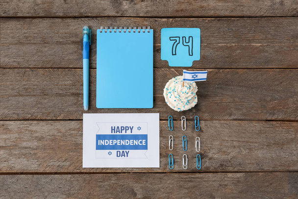 Fournitures de papeterie, cupcake, note collante avec le numéro 74 et carte avec le texte HAPPY INDEPENDENCE DAY sur fond en bois - Photo, image