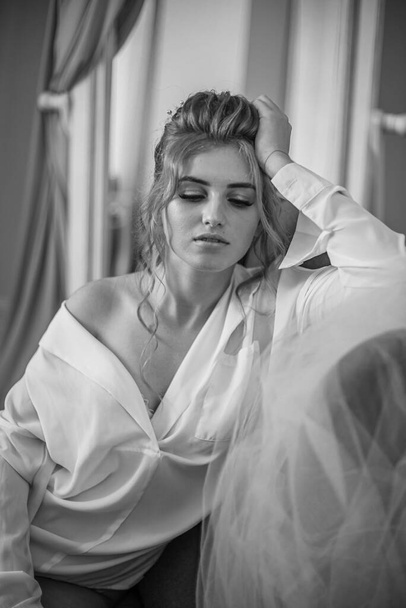 Young beautiful bride with wedding hairdo and makeup in the morning wearing a white silk negligee in the bedroom. wedding morning - Valokuva, kuva
