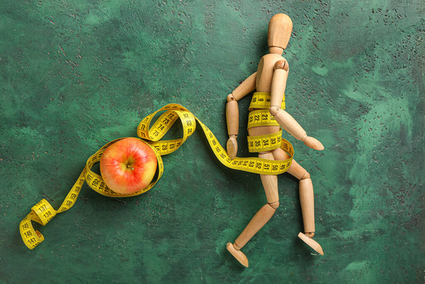 Puinen mallinukke, omena ja mittanauha väritaustalla. Anoreksia käsite - Valokuva, kuva