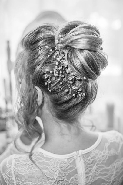 Young beautiful bride with wedding bridal hairstyle with pearls and crystals  near the boudoir table in the bedroom. wedding morning - Fotografie, Obrázek