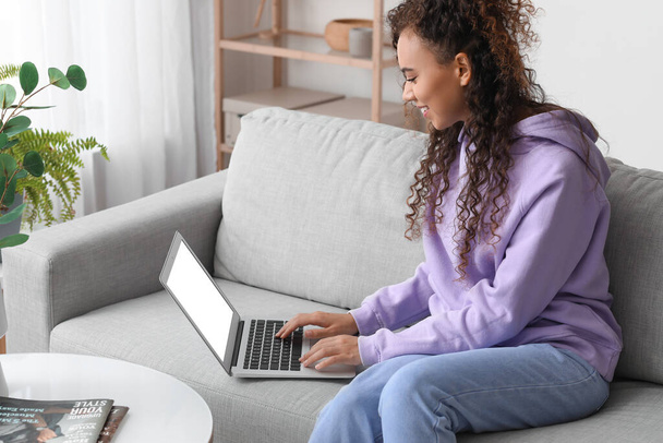 Νεαρή Αφρο-Αμερικανίδα γυναίκα που χρησιμοποιεί φορητό υπολογιστή στον καναπέ στο σπίτι - Φωτογραφία, εικόνα