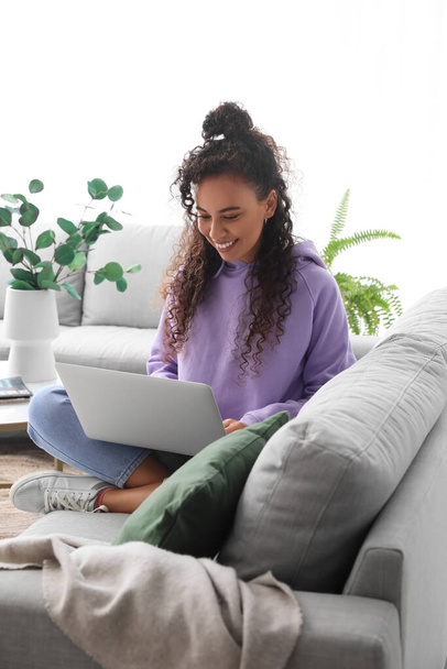 Young African-American woman using laptop on sofa at home - Photo, Image