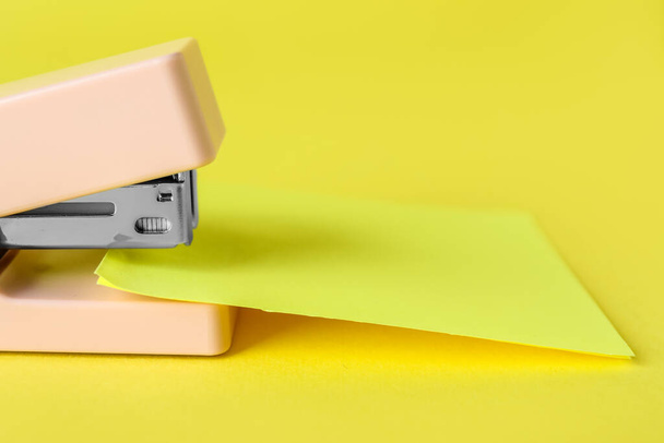Stapler with sheet of paper on yellow background, closeup - 写真・画像