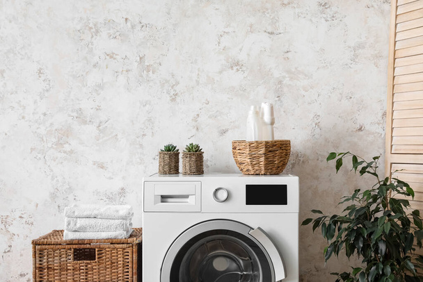 Basket with detergent and houseplant on washing machine near light wall - Foto, immagini