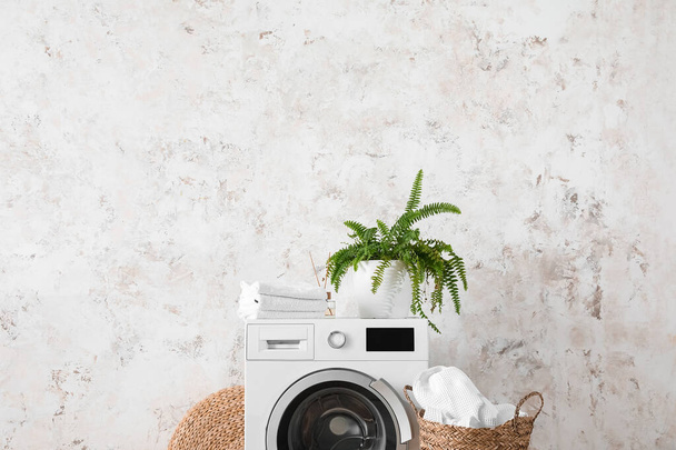 Machine à laver avec serviettes et plante d'intérieur près du mur léger - Photo, image