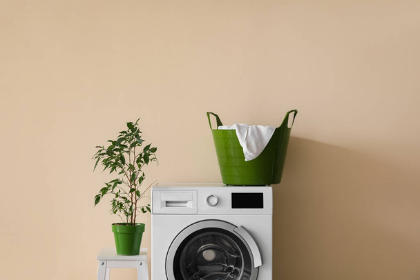 Waschmaschine mit Wäschekorb und Zimmerpflanze auf Leiter nahe beiger Wand - Foto, Bild