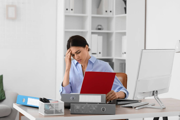 Stressed young businesswoman with folders sitting at table in office - Photo, Image