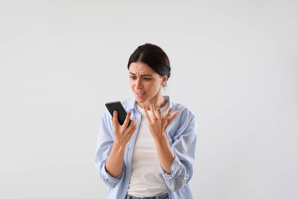 Stressed young woman with mobile phone on light background - Fotoğraf, Görsel