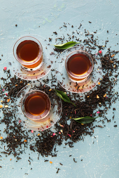 Szklane filiżanki czarnej herbaty i suszone liście na tle koloru - Zdjęcie, obraz