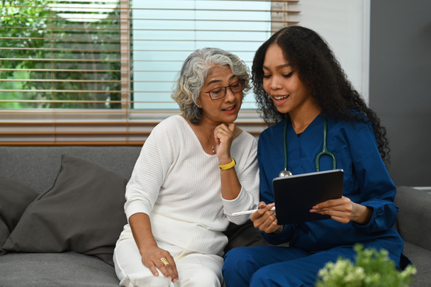 Női orvos kezében digitális tabletta és elmagyarázza a gyógyszer adagját az idősebb nő. Az otthoni egészségügyi szolgáltatás fogalma. - Fotó, kép