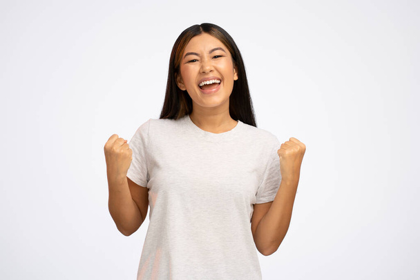 I am champion. Motivated enthusiastic girl screaming for joy and raising high her fists, celebrating successful winning, incredible victory. Studio shot isolated on white background  - Photo, Image