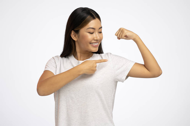 Concept of woman power and independence. Determined brave young lady with brunette hair pointing at biceps, expressing strength and confidence, feminist views. Studio shot isolated on white background  - Photo, Image