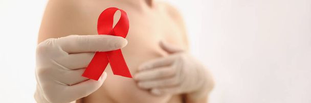 Κοντινό πλάνο της γυναίκας κρατήσει κόκκινη κορδέλα στο χέρι φορούν γάντι, την καταπολέμηση του καρκίνου του μαστού, μήνυμα για τη γυναικεία καταπολέμηση της νόσου. Καρκίνος του μαστού, ιατρική, διαγνωστική έννοια - Φωτογραφία, εικόνα
