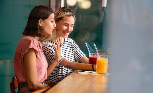 Portrait of two beautiful women having fun, using phone together and chatting in cafe. People happiness technology concept - 写真・画像