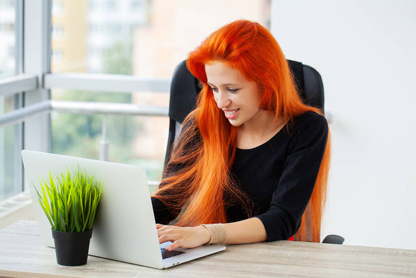 Schöne fröhliche Frau lächelt, während sie im Büro mit Laptop arbeitet. - Foto, Bild